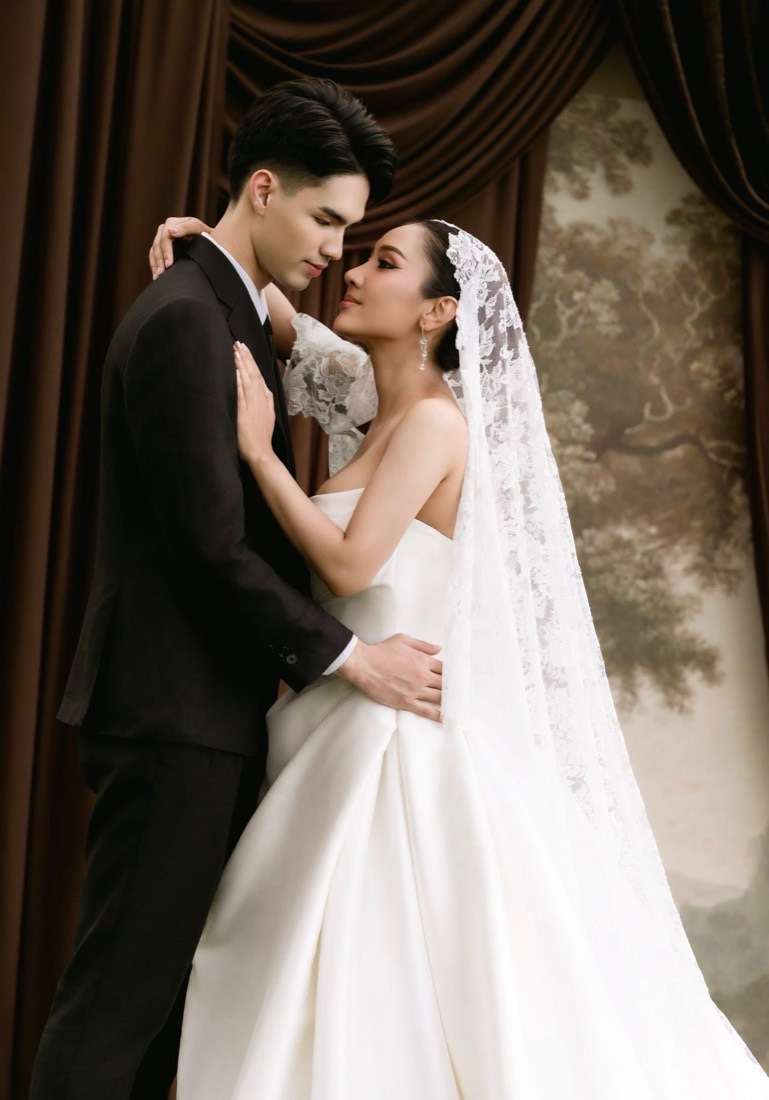 Bride in a draped gown and long veil beside her groom